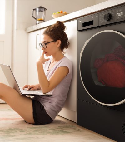 Dziewczyna z laptopem siedzi na podłodze obok suszarki Amica