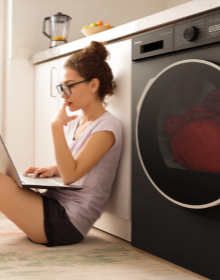 Dziewczyna z laptopem siedzi na podłodze obok suszarki Amica