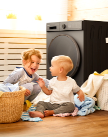 dziewczynka i chłopiec siedzą przy suszarce, na podłodze leżą ubrania
