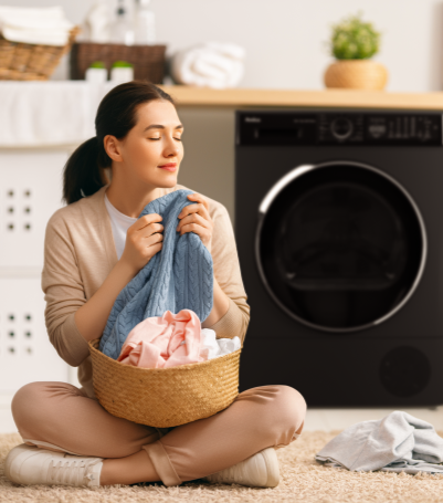 kobieta z praniem siedzi na podłodze, w tle czarna suszarka